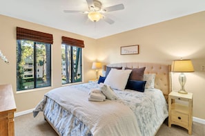 A bedroom with a bed, two bedside tables, a ceiling fan, and a window with blinds.
