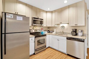 A compact kitchen with a refrigerator, oven, microwave, and a coffee maker. - Soundfront Stay Beach, Pools & More at The Spa (Hilton Head Island)