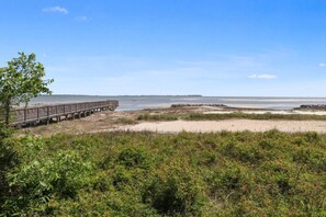A beach with a wooden boardwalk leading to the water, sandy dunes, and sparse vegetation. - Soundfront Stay Beach, Pools & More at The Spa (Hilton Head Island)