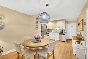 A compact kitchen with modern appliances, a dining area with a round table and chairs, and a hanging light fixture.