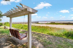 A wooden swing set under a pergola with a view of a beach and a pier. - Soundfront Stay Beach, Pools & More at The Spa (Hilton Head Island)