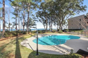 A swimming pool surrounded by trees and a building with a view of the ocean. - Soundfront Stay Beach, Pools & More at The Spa (Hilton Head Island)