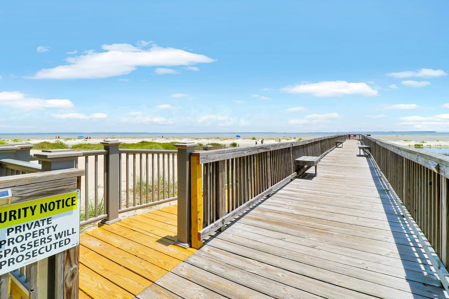 A wooden boardwalk leading to a beach with a security notice sign.