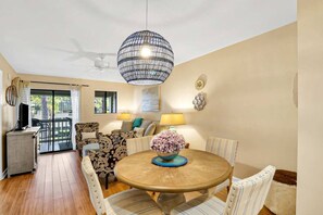 A dining area with a round table, chairs, and a hanging light fixture. - Soundfront Stay Beach, Pools & More at The Spa (Hilton Head Island)