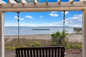 A beach view from a covered area with a bench, a wooden pier, and a rocky outcrop in the distance.