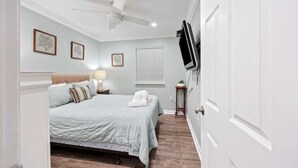 A bedroom with a bed, a ceiling fan, a TV mounted on the wall, and a window with blinds.