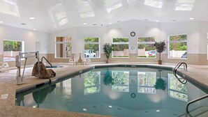 Una piscina interior con ventanas transparentes, una silla de salvavidas y un reloj en la pared.