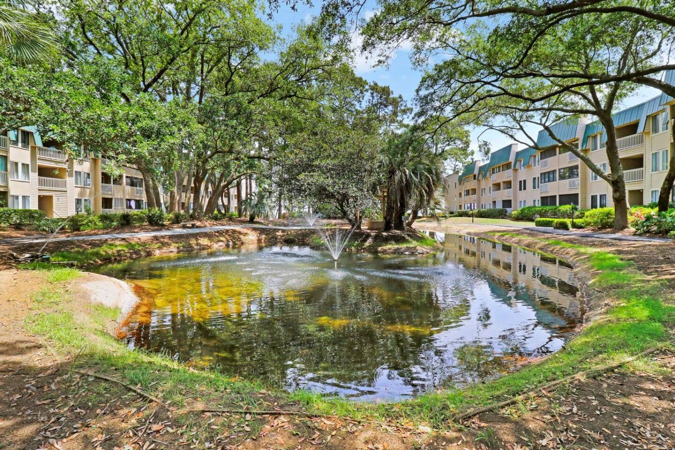 Un patio central con un estanque, rodeado de árboles y edificios de varios pisos con balcones.