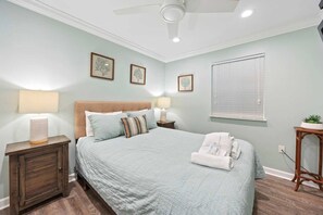 A bedroom with a bed, bedside lamps, a nightstand, a ceiling fan, and a window with blinds.