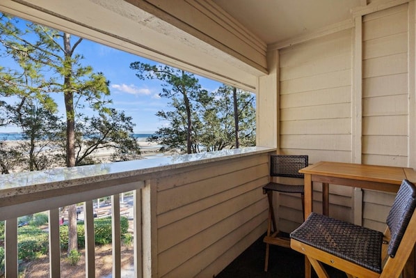 Un balcon avec vue sur la plage et l’océan, une table en bois et deux chaises en osier.