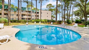 A swimming pool with lounge chairs and a no diving sign, surrounded by trees and a building.