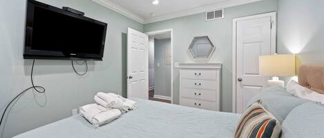 A bedroom with a bed, a television mounted on the wall, a dresser, a mirror, and a lamp.