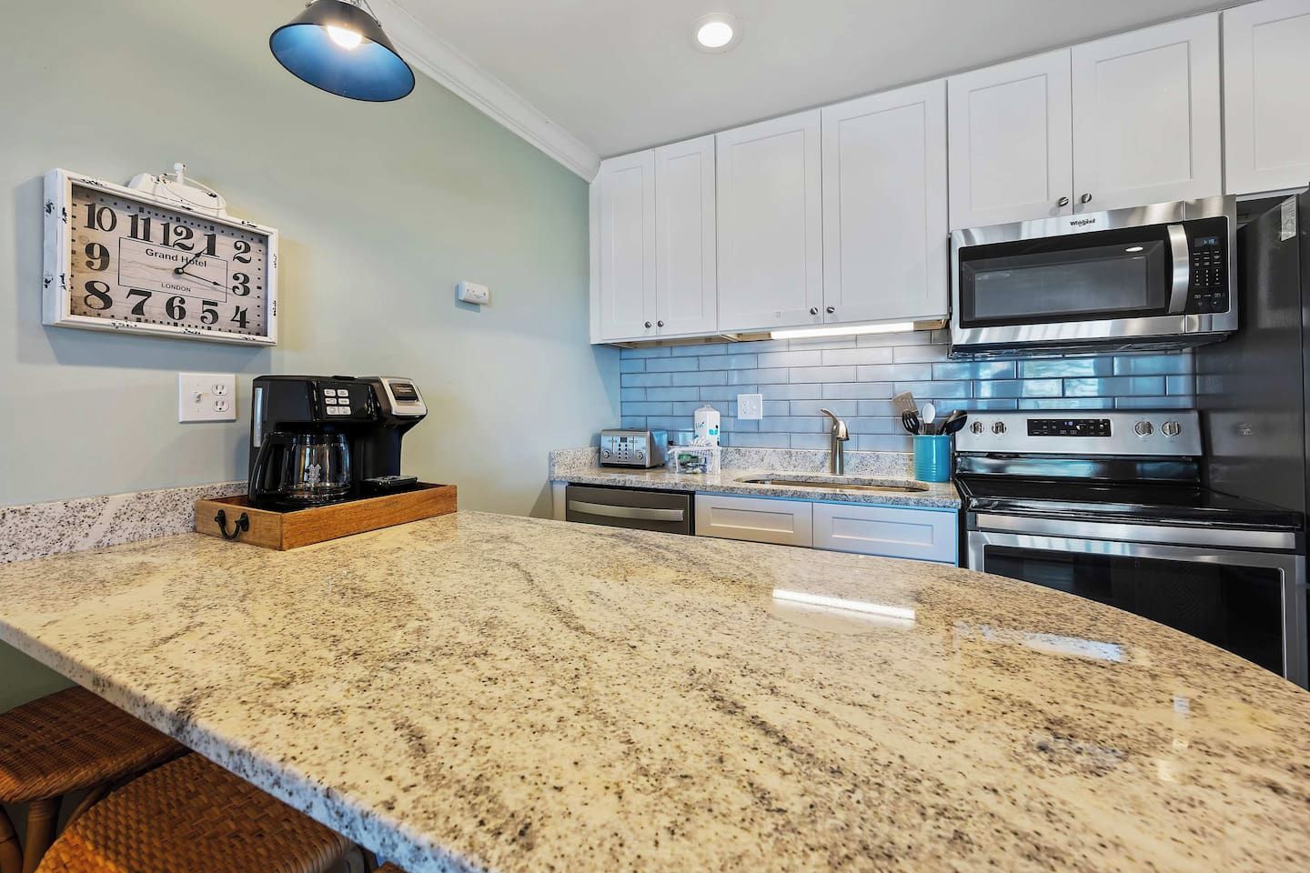 A kitchen with granite countertops, stainless steel appliances, white cabinets, and a coffee maker.