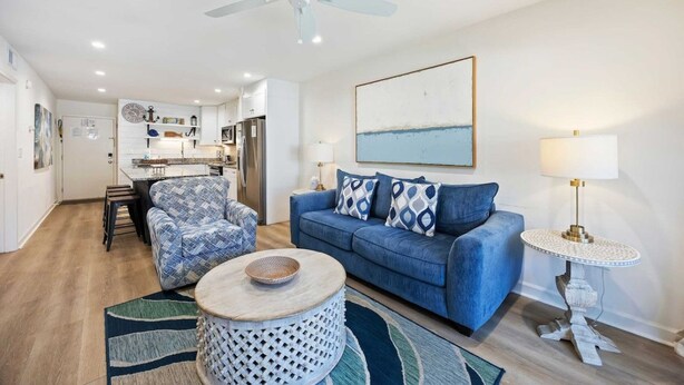 Una sala de estar moderna con un sofá azul, una mesa redonda y un comedor con una cocina al fondo.