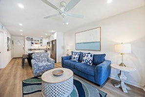 A modern living room with a blue sofa, a round coffee table, and a dining area with a kitchen in the background.