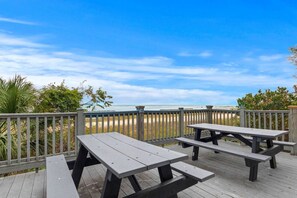 Une terrasse en bois avec des tables de pique-nique donnant sur une plage.