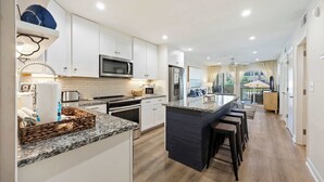 Una cocina moderna con armarios blancos, encimera de granito y una isla central con taburetes de bar.