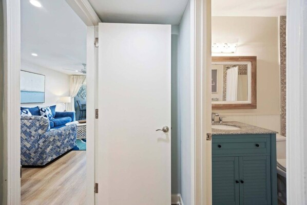 A room with a bed, a bathroom with a sink and mirror, and a door leading to another room.