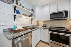 A modern kitchen with white cabinetry, a stainless steel dishwasher, a built-in oven, a microwave, and a granite countertop.