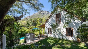 A white house with a patio, surrounded by lush greenery and a mountain in the background. - ZenCapeTown Holiday House (Cape Town)