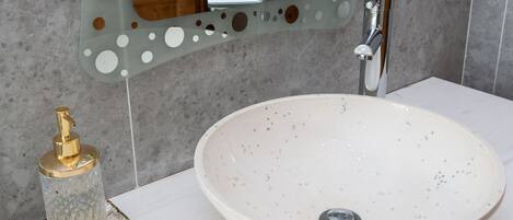 A bathroom with a white sink, a gold soap dispenser, and a mirror with circular cutouts.