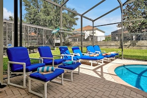 Zona junto a la piscina con sillas reclinables azules y una zona de estar cubierta.