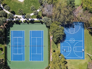 Vista aérea de un complejo de canchas de tenis con dos canchas, rodeado de árboles y un sendero para caminar.