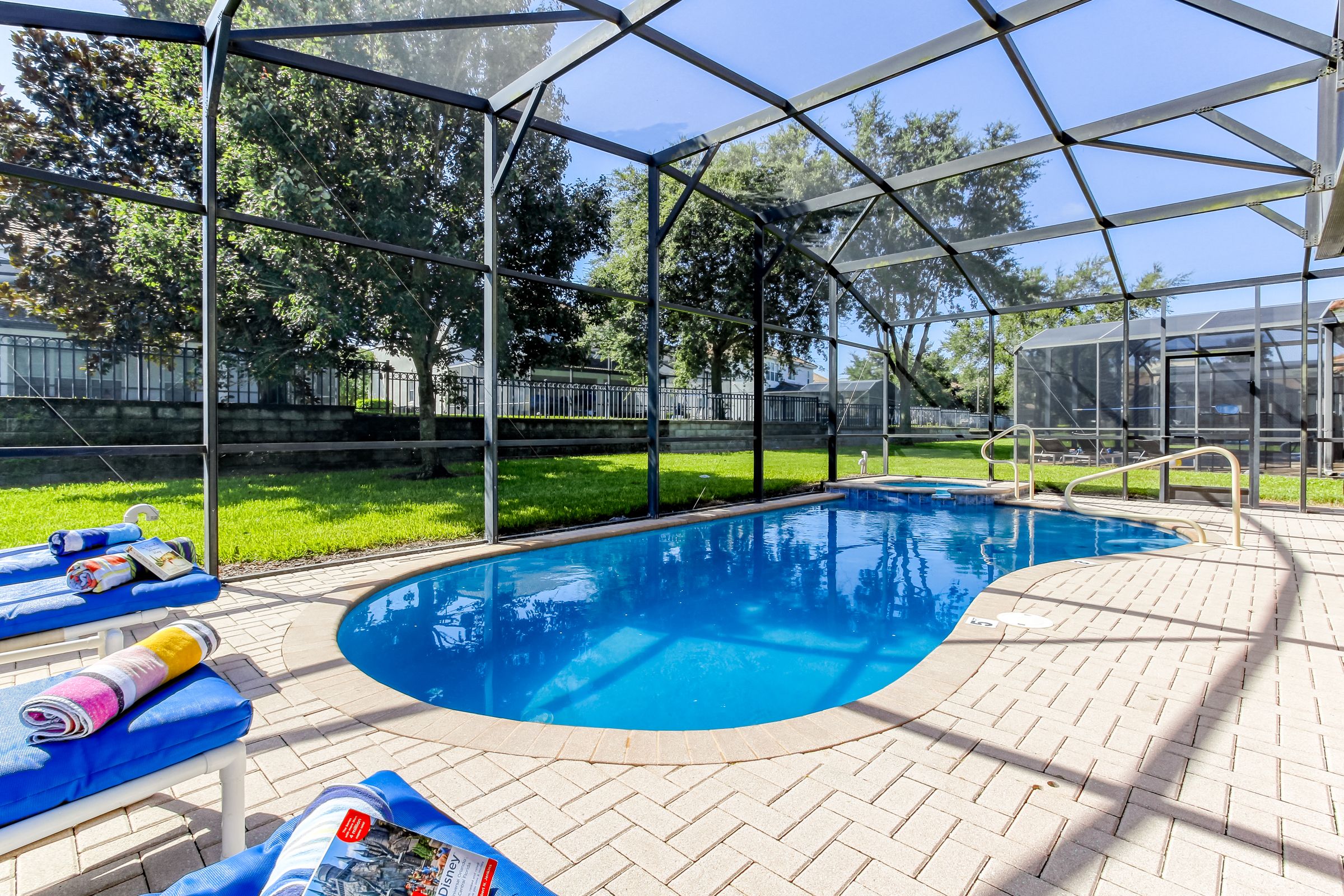 A swimming pool with a glass enclosure, surrounded by a brick patio, and equipped with lounge chairs and towels.