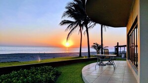 Un patio con vistas a la puesta de sol sobre el océano, palmeras y un edificio con ventanas amplias.