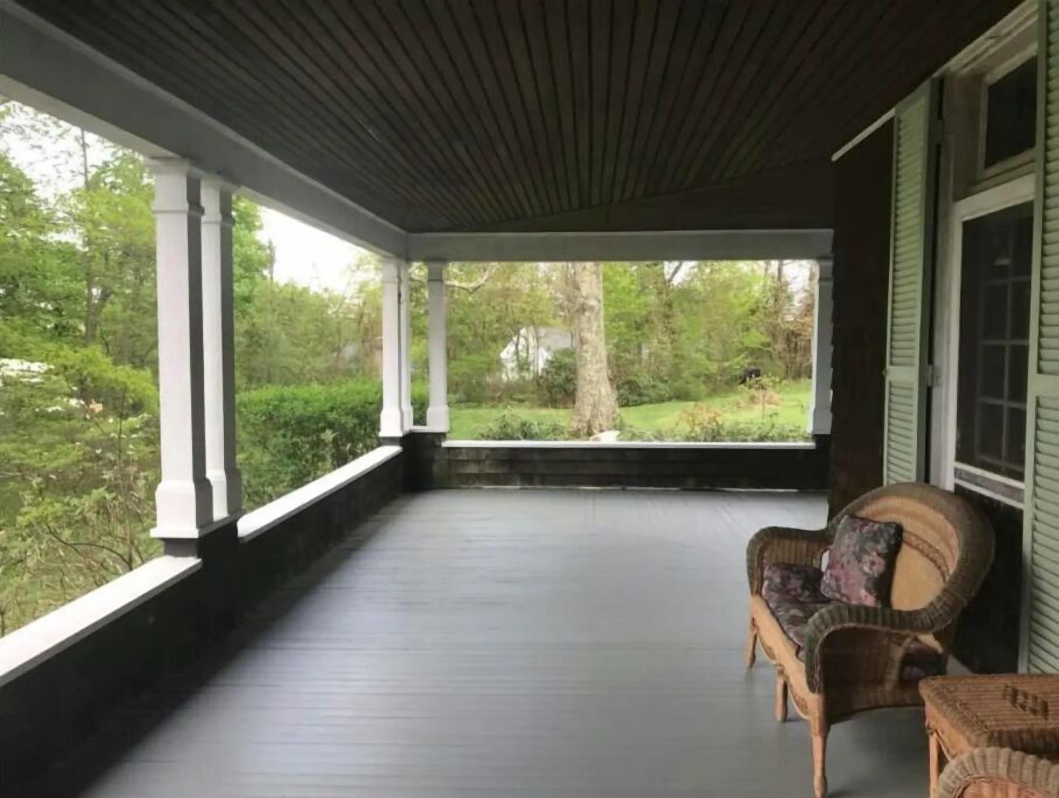 Un porche cubierto con piso de madera oscura, columnas blancas y mobiliario de mimbre.