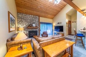 A cozy living room with a stone fireplace, leather sofas, a wooden table, and a television. - Luxury Snowcreek Home w/ Mountain Views! (Mammoth Lakes)
