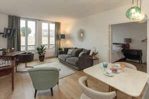 A modern living room with a sofa, dining table, and chairs. There is a TV mounted on the wall, a potted plant, and a decorative mirror. - Chantilly Cocoon Retreat (Chantilly)