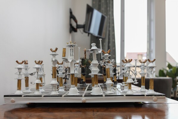 A chessboard with pieces on a table in a room with a TV and curtains in the background. - Chantilly Cocoon Retreat (Chantilly)