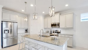 A modern kitchen with white cabinetry, stainless steel appliances, a granite countertop, and a central island with bar stools. - *NAPLES HOUSE WITH POOL near Marco Island (Naples)