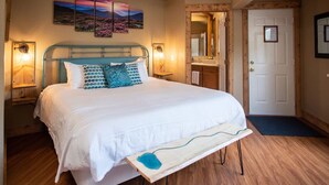 A bedroom with a bed, bedside lamps, a wooden floor, a large mirror, and a door.