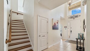 Una scala con gradini in legno che conduce a un pianerottolo, una porta bianca con serratura di sicurezza, un cartello di benvenuto sopra una porta e un tavolino con un cartello di benvenuto sopra.