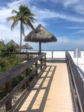 A wooden boardwalk leading to a beach with thatched umbrellas and a palm tree. - Marco Island Waterfront Condo  (Marco Island)