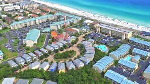 Vue aérienne d’une station balnéaire comprenant plusieurs bâtiments, une plage et un parking.