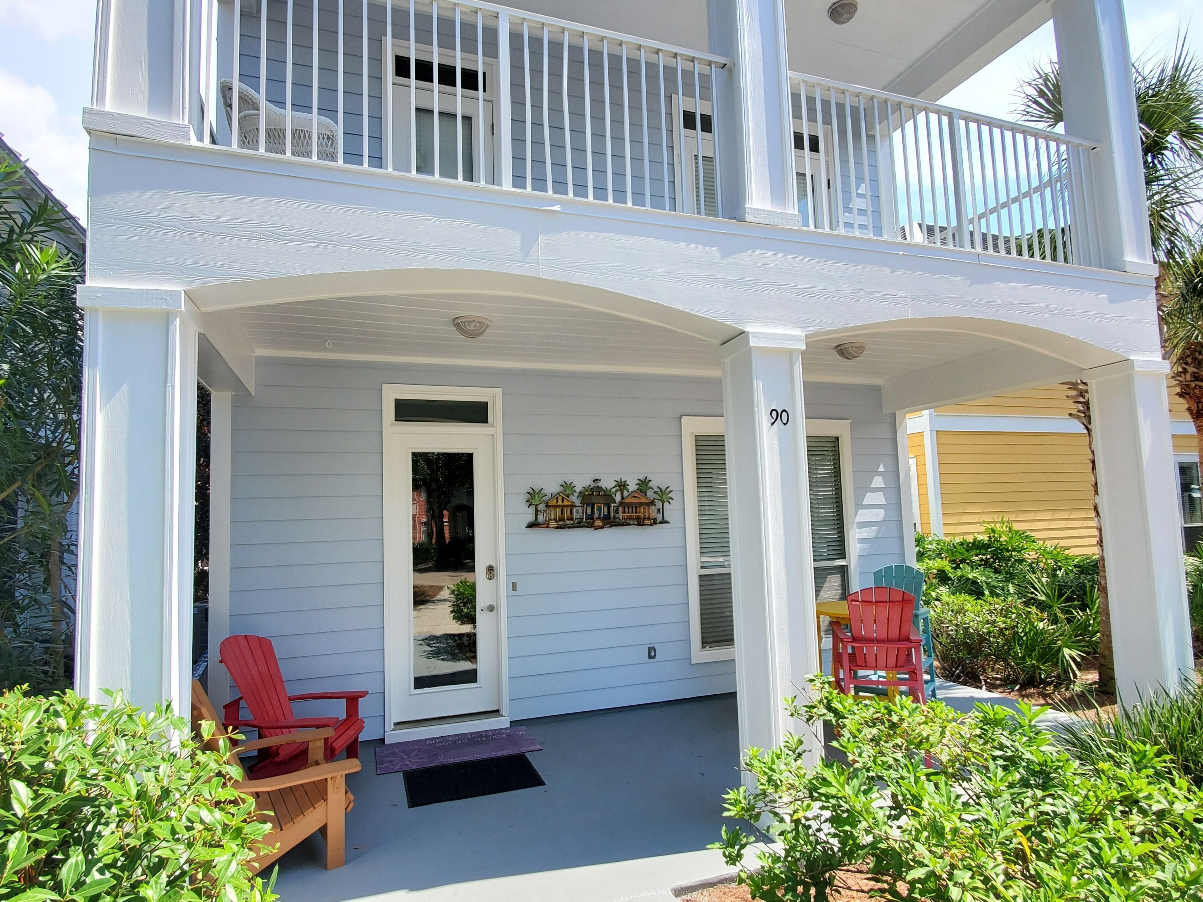 A two-story house with a covered porch, a door with a glass panel, and a small outdoor seating area with chairs.