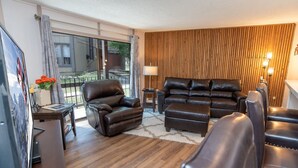 A modern living room with leather sofas, a wooden floor, and a large window overlooking a balcony. - Gold Camp Miners' Inn Condo: Nice Location, Updates (Breckenridge)