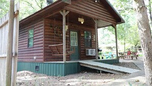 A rustic log cabin with a porch, a swing, and a ramp leading to the entrance. - One Bedroom with Loft Sleeps Six By Cedar Creek Golf Course & Broken Bow Lake (Broken Bow)