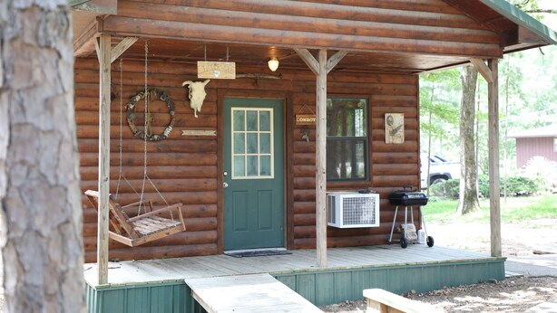 A rustic cabin with a porch, a swing chair, a door with a window, and a sign that reads "COWBOY". - One Bedroom with Loft Sleeps Six By Cedar Creek Golf Course & Broken Bow Lake (Broken Bow)