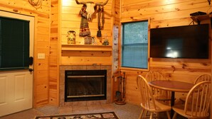 A cozy cabin interior with a fireplace, wooden walls, a mounted cow skull, and a TV. - One Bedroom with Loft Sleeps Six By Cedar Creek Golf Course & Broken Bow Lake (Broken Bow)