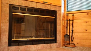A fireplace with a glass door, a wooden mantel, and a bell in a room with wooden walls and a tiled floor. - One Bedroom with Loft Sleeps Six By Cedar Creek Golf Course & Broken Bow Lake (Broken Bow)