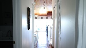 Um corredor com piso de azulejos, teto de madeira e uma porta branca à direita.