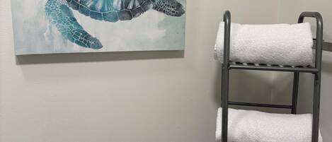 A bathroom with a towel rack holding white towels, a toilet paper holder, and a painting of a sea turtle.