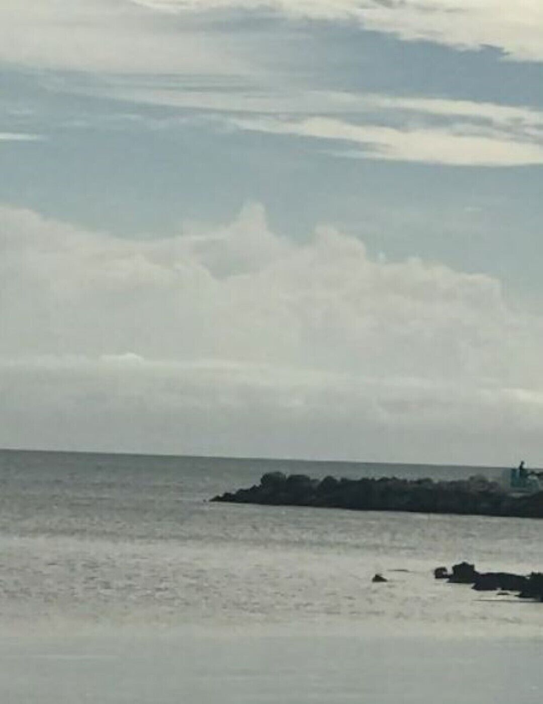 A coastal view with a rocky shoreline and a lighthouse in the distance.