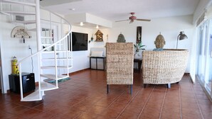 Uma sala de estar ampla com escada em espiral, móveis de vime e um ventilador de teto.