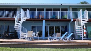 Hotel com varanda de dois andares, área de estar externa com cadeiras e mesas, e espaço na piscina com espreguiçadeiras.