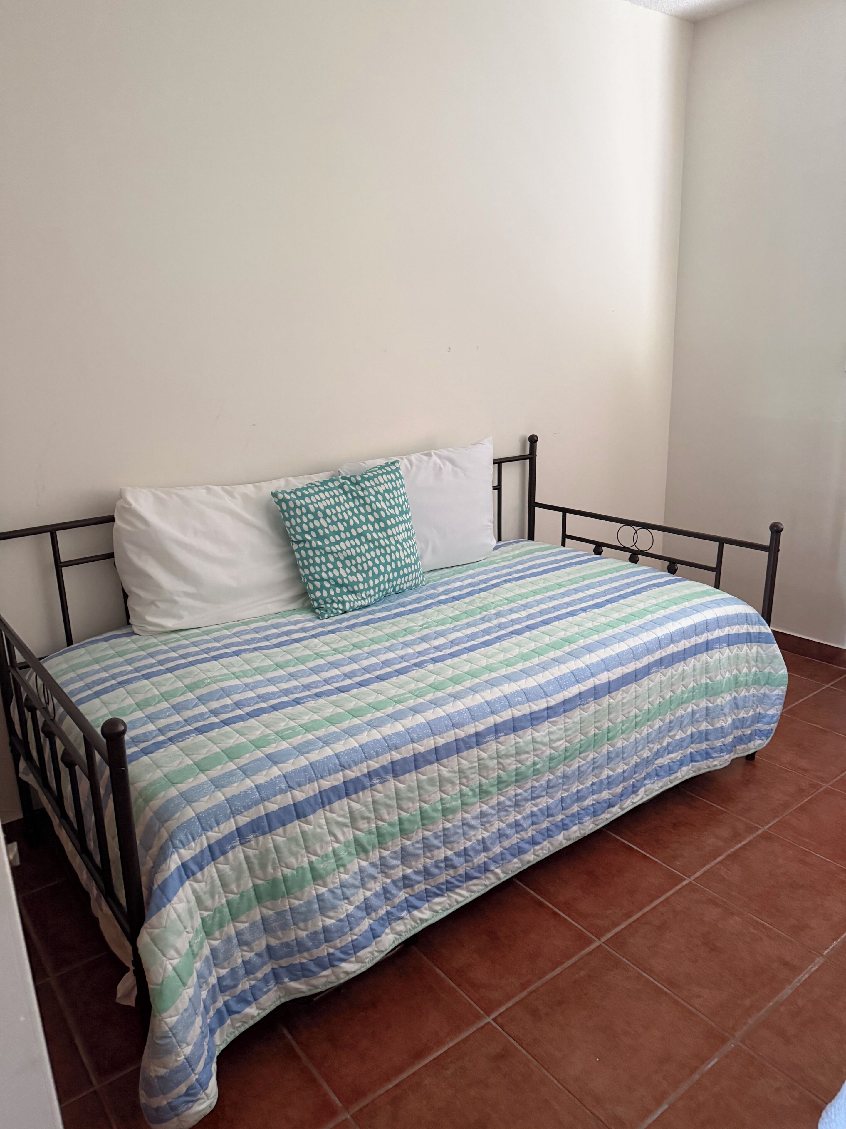 Una cama individual con una colcha a rayas, un almohadón blanco y un almohadón verde con lunares.